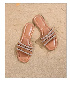 Detail von böhmischen flachen Sandalen mit funkelnden Strasssteinen auf braunem Sandstrand