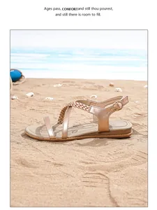 Detail of rose gold T-strap flat sandal with braided strap and buckle on a beach