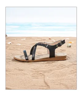 Detail of bohemian flat sandals featuring black braided straps on a sandy beach background
