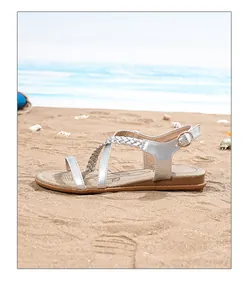 Detail of silver bohemian flat sandals with braided straps on a sandy beach background