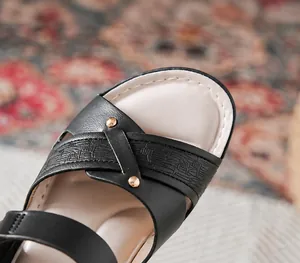 Detailansicht der weichen schwarzen Lederriemen mit goldenen Metallnieten am Schuh