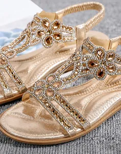 Detailed shot of champagne gold flat sandals with floral rhinestones and microfiber fabric