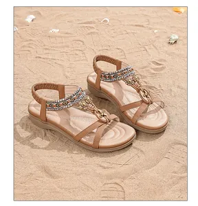 Détail de sandales bohèmes beige avec perles et fleurs en métal sur une plage de sable