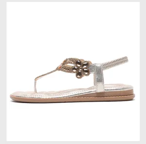 Detaillierte Seitenansicht flacher champagnergoldener Sandalen mit Strassblumen-Verzierung