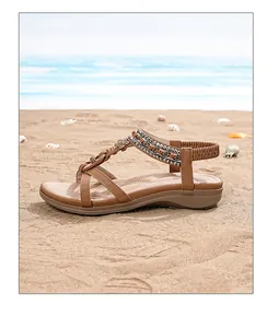 Détail de sandale bohème marron avec perles et fleur en métal posée sur le sable