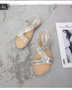 Détail de sandales plates argentées avec fleurs en strass et semelle intérieure aspect bois