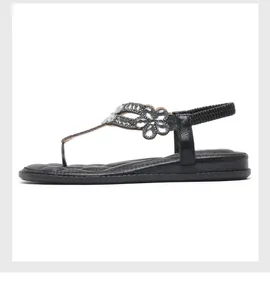 Detail von schwarzen flachen Sandalen mit Strassblumen und elastischem T-Riemen