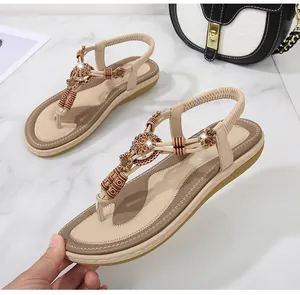 Detail of beige flat sandals featuring 3D floral accents and wooden beads on marble
