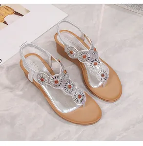 Dettaglio di sandali con zeppa argento con cinturino a T e decorazioni in strass floreali