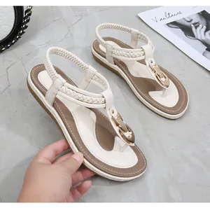 Detail of cream thong sandals featuring woven straps and golden buckle on marble background