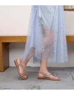 Détail de sandales plates or rose avec motif floral en strass sur le pied d'un mannequin