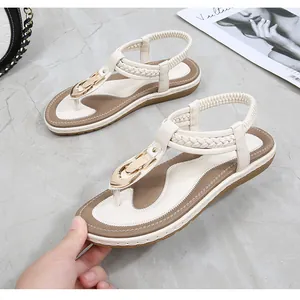 Detail view of white thong sandals with gold buckle on marble floor backdrop
