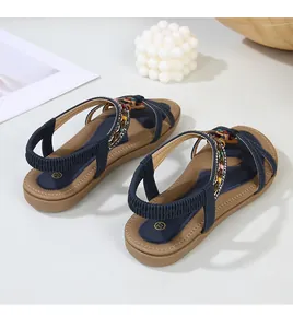 Detail view of navy blue flat sandals featuring cross straps, beads, and elastic heel strap