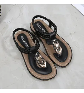 Detail of black T-strap sandals featuring large gold metal buckle and woven elastic strap