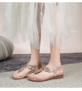 Detailansicht goldener flacher Sandalen mit Strasssteinen und T-Riemen am Fuß getragen