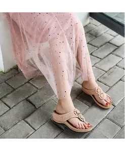 Détail de sandales compensées beige avec brides ajourées et fleurs portées par le modèle