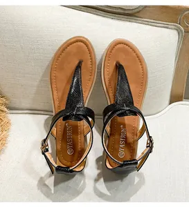 Detailed top view of black T-strap flat sandals with snake texture and brown insoles