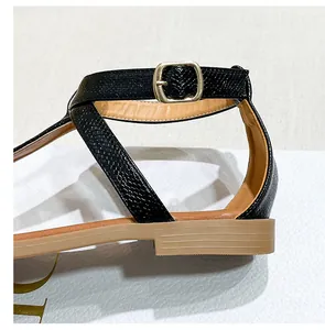 Detail of black faux-snakeskin T-strap sandals with gold buckle and flat heel