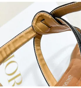 Detail of black snakeskin texture leather strap with white contrast stitching on flat sandals