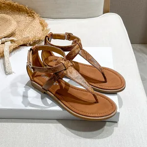 Detail of brown T-strap flat sandals with snake pattern texture and buckle closure