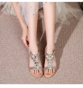 Detailed close-up of champagne gold flat sandals with sparkling rhinestone T-strap design