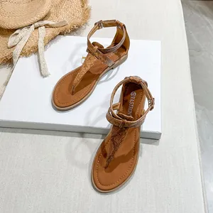 Close-up of brown snakeskin flat sandals with T-strap and buckle details on a white stand