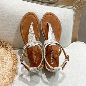 Flat gladiator sandals with snake print straps and metallic buckle on a resort background