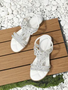 Detail of white bohemian flat sandals with rhinestone butterfly patterns on wood and stones