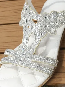 Detailed macro view of white flat sandals featuring sparkly rhinestones and quilted footbed