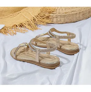 Detail goldener flacher Sandalen mit Strass-T-Riemen auf weißem Satintergrund