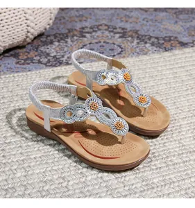 Detailaufnahme silberner Boho-Sandalen mit orangen Blumen auf einer geflochtenen Matte