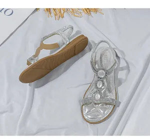 Nahaufnahme silberner T-Steg-Sandalen mit Strasssteinen und weißen Perlenverzierungen