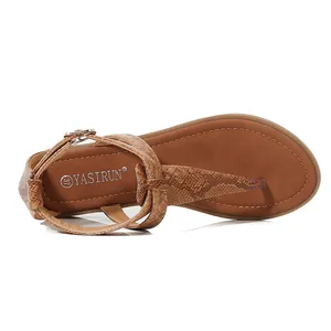 Macro detail of brown faux leather T-strap sandals with snake texture and buckle closure