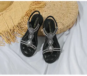 Nahaufnahme schwarzer T-Riemen Sandalen mit Strass und grauen Steinen auf Strohmatte
