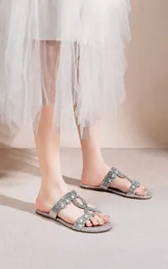 Détail de sandales plates argentées avec des ornements en strass et perles sur les brides