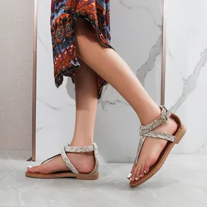 Detail of tan snakeskin flat sandals with adjustable ankle straps on a model feet