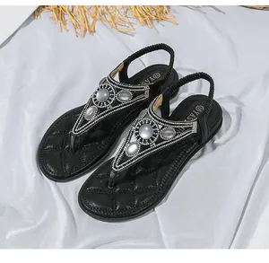 Dettaglio di sandali bassi neri con cinturino a T con strass e gemme su raso bianco