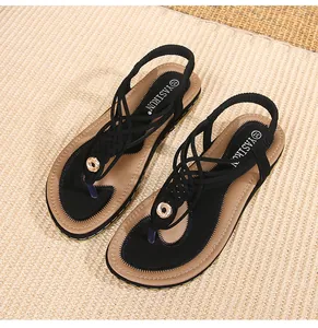 Détail de sandales noires plates style bohème avec boucle dorée sur tapis tressé