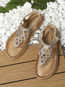 Detail einer flachen Boho-Sandale mit aufwendigen goldenen Perlen und funkelnden Strasssteinen