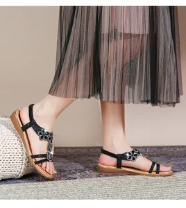 Nahaufnahme schwarzer flacher Sandalen mit floralen Strassdetails und Goldrandsohle