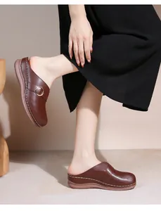 Détail de mules en cuir marron avec motifs ajourés et boucle en métal doré