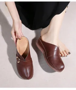 Détail de mules marron foncé à découpes avec boucle dorée et cuir perforé respirant