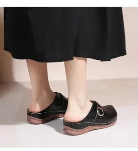 Gros plan de mules en cuir noir avec boucle dorée et coutures blanches sur la semelle