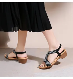 Dettaglio di sandali con zeppa neri con strass a T e tacco in texture legno indossati