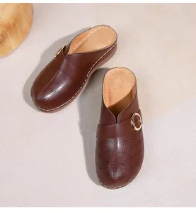 Détail de mules en cuir marron avec perforations et boucle dorée décorative