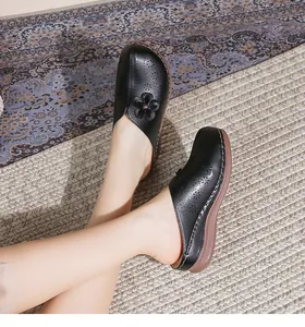 Close-up of black hollow-out floral leather sandals with thick wedge soles and hand-stitching