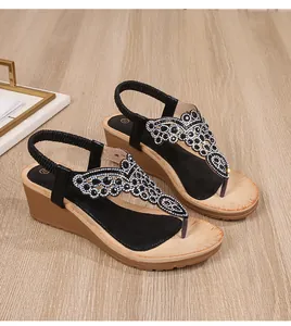 Close-up of black bohemian wedge sandals with rhinestone butterfly detail on wooden floor