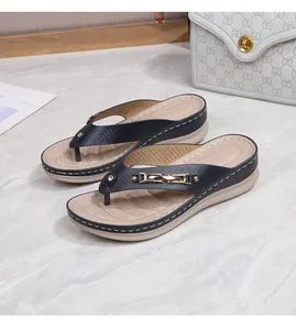 Close-up of black thong sandals with gold buckle detail and beige platform wedge heel
