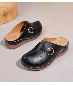 Détail de mules noires ajourées avec boucle dorée et semelle compensée souple