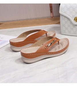 Detail of brown wedge flip flops with gold metal chain and textured footbed on marble